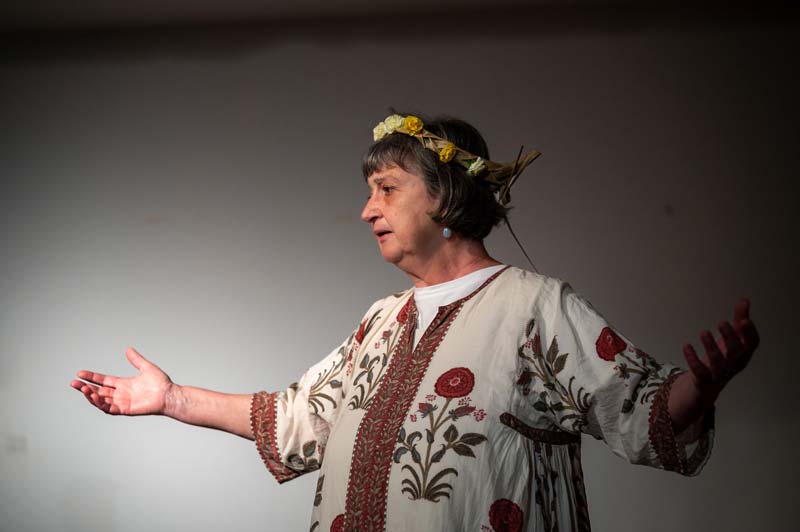 Luisa no papel de Deméter, de braços abertos e coroa de flores, em cena.